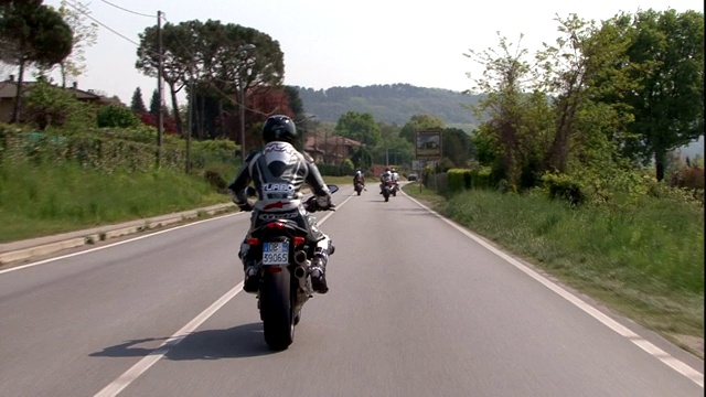 在乡村道路上，摩托车手们骑着摩托车经过一户人家。视频素材
