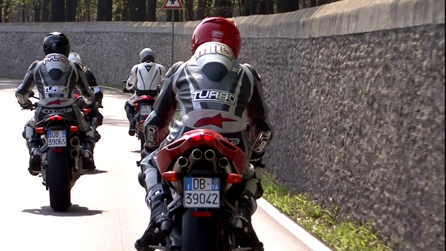当摩托车手在一堵石墙旁骑时，摩托车手会给手势。视频素材