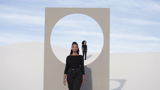 在沙漠中，妇女们站在有圆形窗框的广告牌旁视频素材