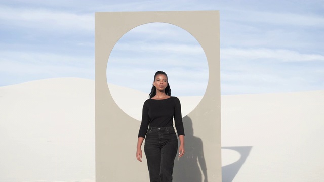 在沙漠中，一个女人走在有圆形窗框的广告牌前，视频素材