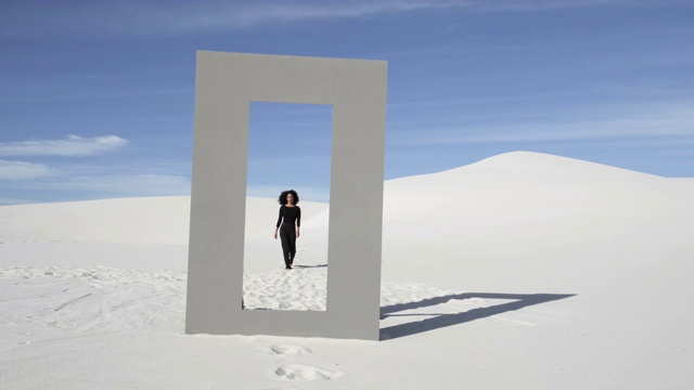 一头卷发的女人在沙漠中穿过门框，很宽视频素材