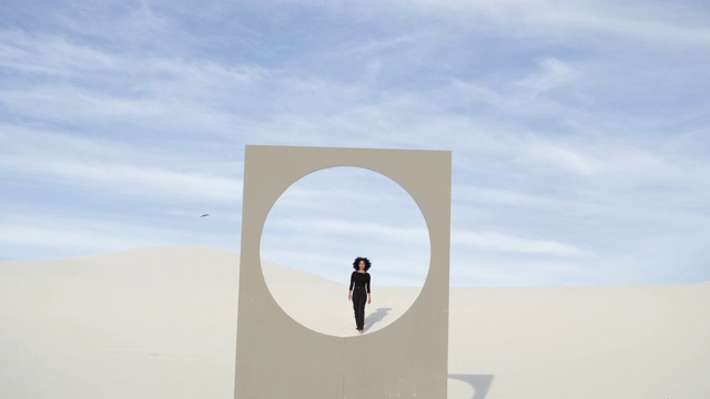 沙漠中，女子走到有圆形窗框的广告牌前，中景视频素材