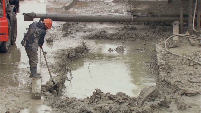 建筑工人站在一个泥泞的洞附近。视频素材