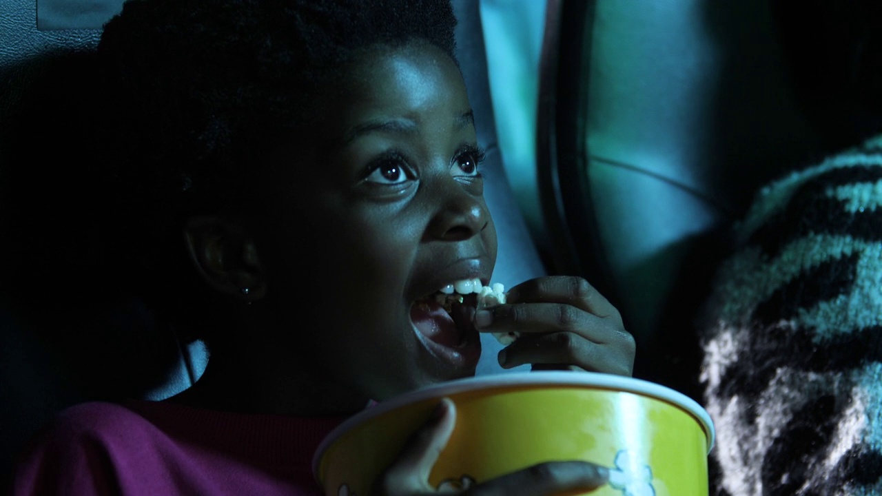 惊奇的年轻非洲裔美国女孩在电影院拿着爆米花，特写视频下载