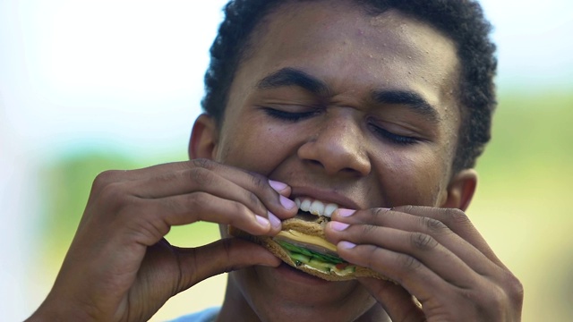饥饿的美国黑人少年吃着美味的三明治，午餐刹车在学校视频下载