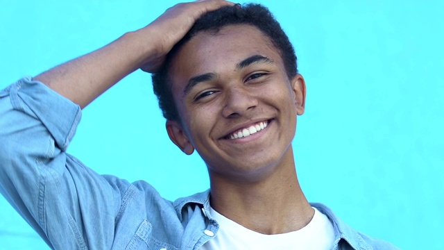 一个积极的非洲裔美国少年在蓝色背景下对着照相机笑视频下载