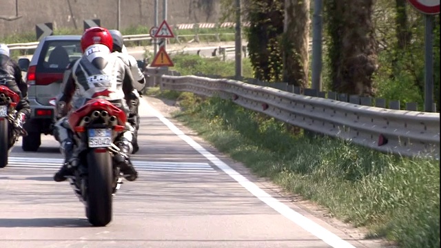 在一条狭窄的道路上，摩托车手们成群结队地跟着一辆汽车行驶。视频素材