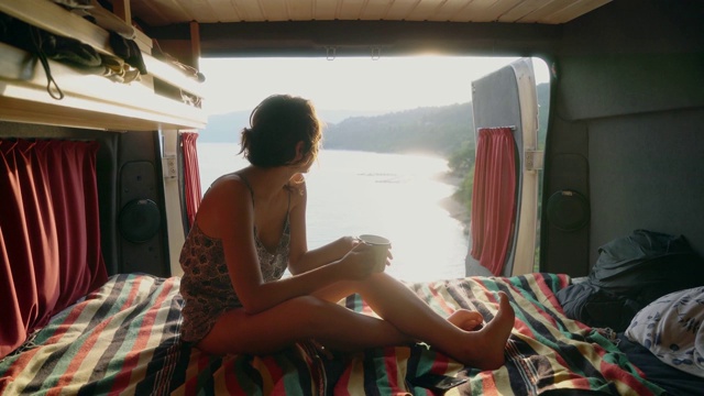 女人看着圣克罗伊湖，在露营车里喝茶视频下载