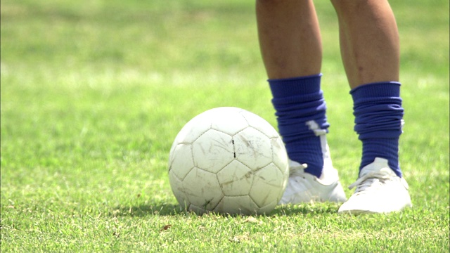 一个足球运动员系上他的球鞋，开始在草地上踢足球。视频素材