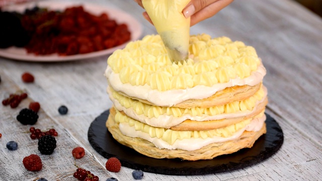 女糕点师用挤花袋和旋转蛋糕架在家庭厨房的桌子上用奶油糖霜装饰蛋糕。视频下载