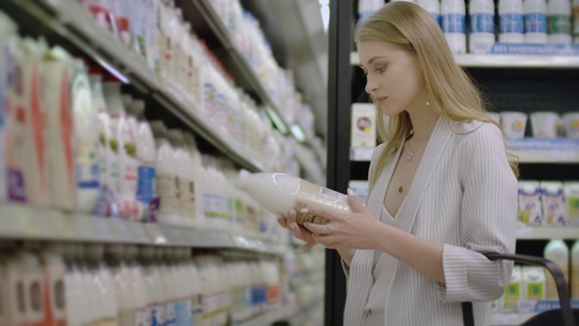 一个女人沿着冰箱走，选择了一瓶牛奶，拿起标签看了看视频素材