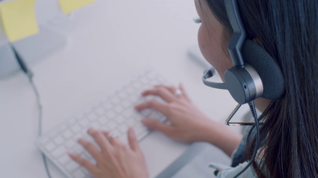 在一个年轻的亚洲女人工作在一个呼叫中心的肩膀，特写视频素材