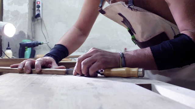木匠用凿子用燕尾榫雕刻木头。木工在木工车间里为木制部件做燕尾榫接头。4 k。4 k的视频。缓慢的运动。24帧/秒视频素材