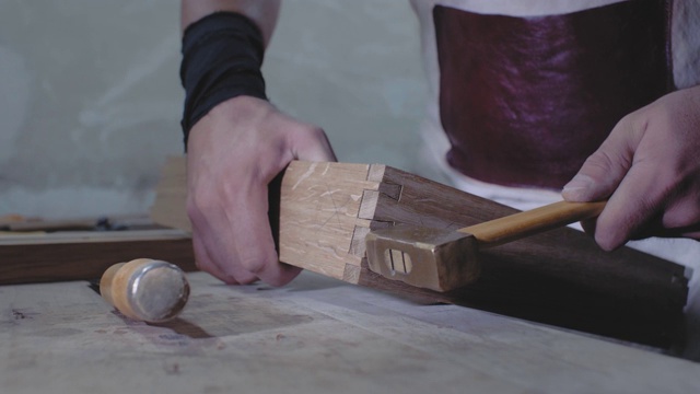 木匠用锤子将用燕尾技术制成的两个木制部件连接起来。一个木匠用燕尾榫接合的细节。4 k。4 k的视频。缓慢的运动。24帧/秒视频素材