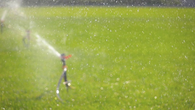 慢动作花园灌溉喷灌机浇灌草坪散焦视图视频素材