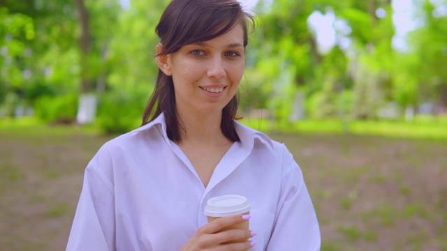 近距离观察穿着白衬衫在街上喝咖啡的年轻女性视频下载