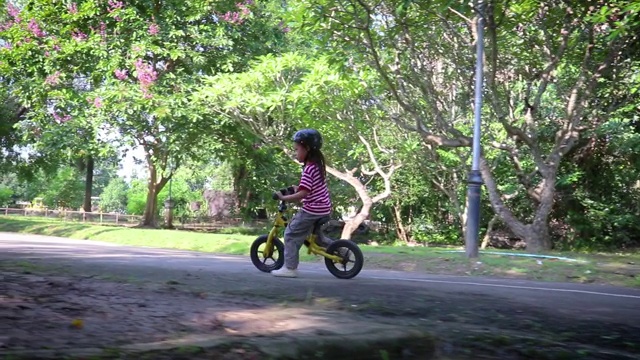 孩子们骑着自行车平衡地在柏油路上穿过公园的小溪。视频素材