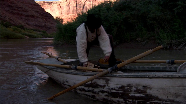 在科罗拉多河的岸边，三个穿着旧式西部服装的男人从一只木制划艇里爬出来。视频下载