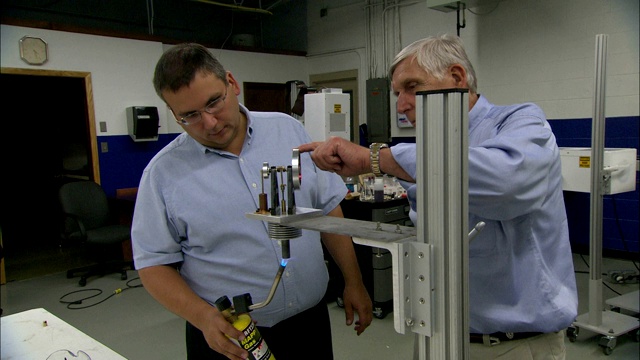 一位科学家转动一个小装置上的轮子，而他的同事则拿着一个小火炬将其底部点燃。视频素材