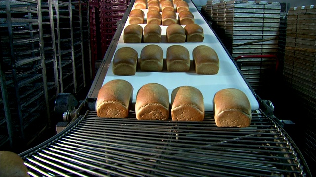 在面包工厂里，面包从传送带上传到移动的货架上。视频下载
