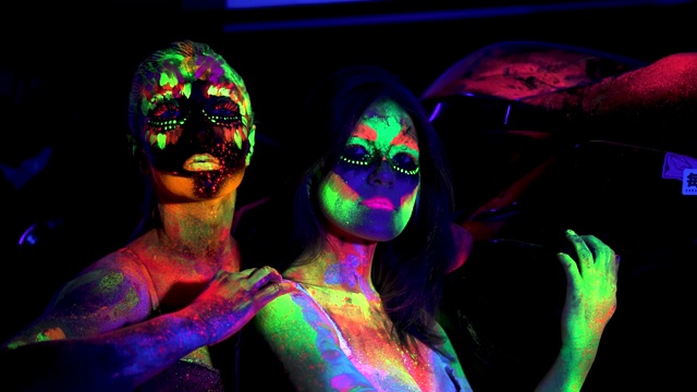 在夜店的紫外线灯下，两个穿着未来主义荧光人体艺术的女孩视频下载