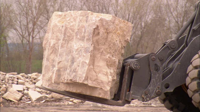 在采石场，一台重型设备搬运着一块巨大的石灰石板。视频素材