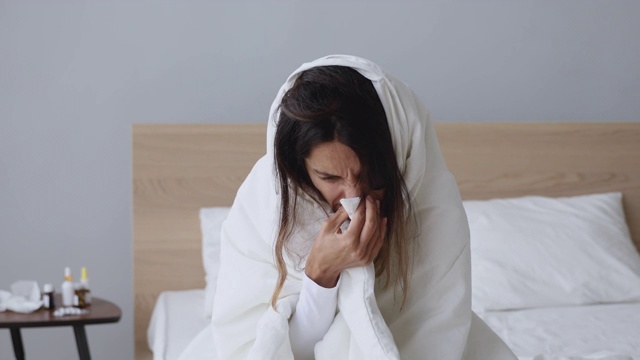 生病的年轻女子浑身裹着毯子，擤着鼻子，得了流感视频素材
