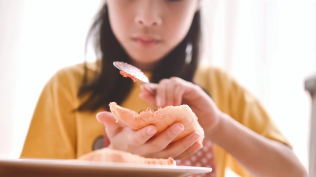 亚洲妹妹为妹妹在面包上涂草莓酱。视频下载
