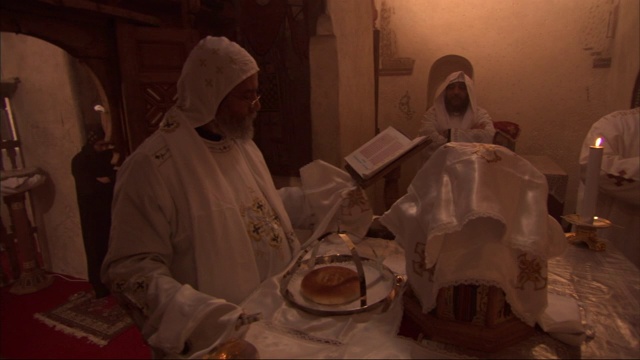 几名身穿白色礼服的埃及男子在教堂祭坛周围走来走去，祭坛上装饰着食物、蜡烛和布料，似乎是在准备一场仪式。视频下载