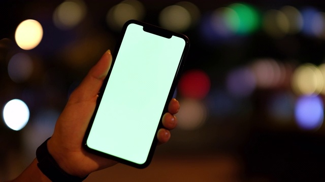 靠近一个在晚上显示绿色屏幕智能手机的人。视频素材