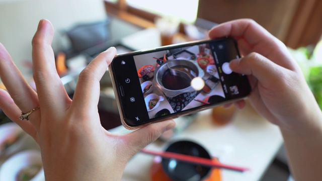 白天，在一家餐馆里，一位女士的手正在用智能手机拍摄日本火锅视频下载