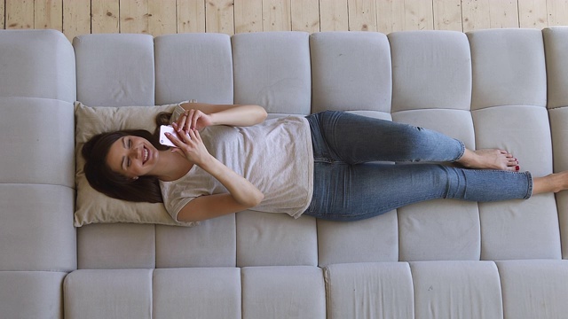 开心放松的女孩用手机躺在沙发上，俯视图视频下载