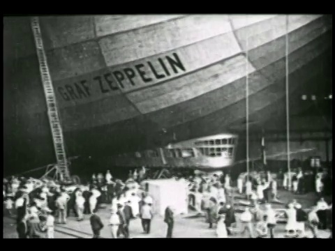一段古德伊尔的视频显示，在新泽西州的一个飞机库中，成千上万的人在齐柏林爵士号和洛杉矶号的巨型飞艇下行走。视频素材