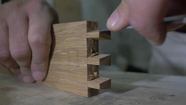 特写，木匠在一个工作台上用凿子在木头上做一个燕尾。木工处理橡木细节。4 k。4 k的视频。缓慢的运动。24帧/秒视频下载