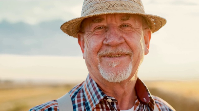 一个快乐的白人农民在麦田里对着镜头微笑，然后摘下了他的帽子。关闭了。视频下载