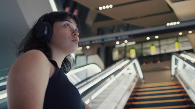 日本东京，一名年轻的日本女子戴着耳机在夜间乘坐自动扶梯视频下载