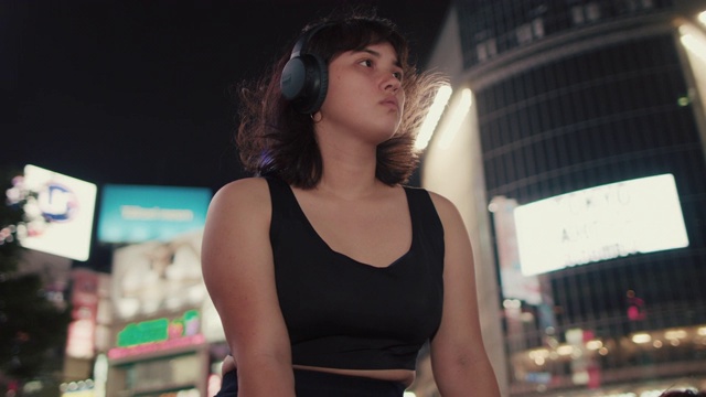 日本东京，一名年轻的日本女子戴着耳机坐在繁忙的广场上视频素材