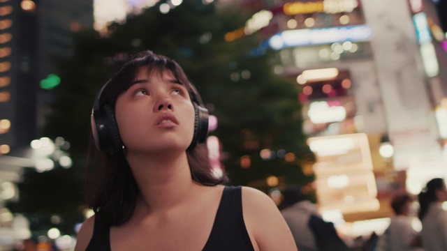 年轻的日本女人戴着耳机在晚上看城市/东京，日本视频下载
