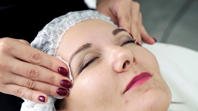 在脸部护理程序前，美容师用湿棉垫清洁女性皮肤视频下载