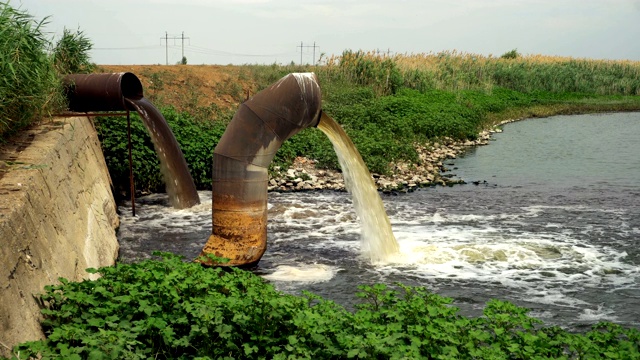 两条生锈的大管道排出的废水以一团团蒸汽的形式汇入河中视频素材