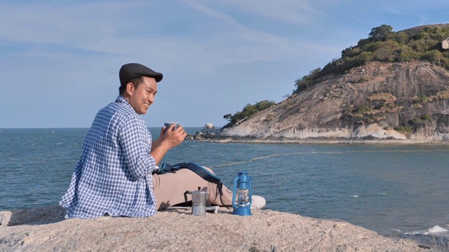 快乐的亚洲男人拿着咖啡杯与自然背景，露营概念。缓慢的运动。视频下载