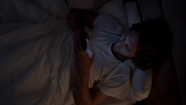 一名男子在睡觉前用手机上网视频下载