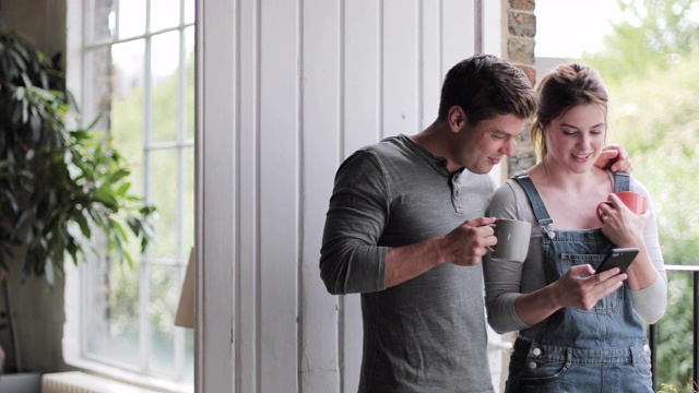 年轻的夫妇在早上喝咖啡，看手机视频素材
