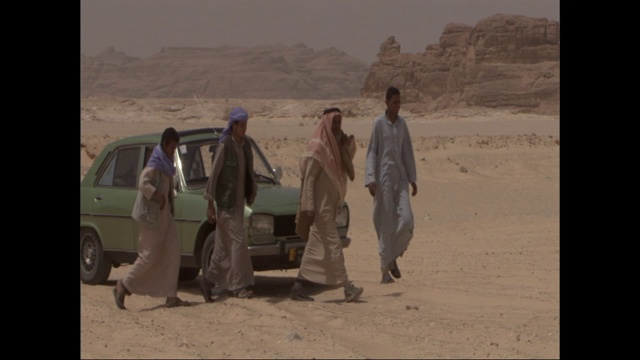 穿着长袍的埃及人在沙漠中从一辆汽车旁走开。视频下载