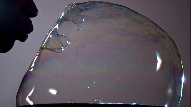 一个人吹一个泡泡，使它在慢动作中扭曲。视频素材