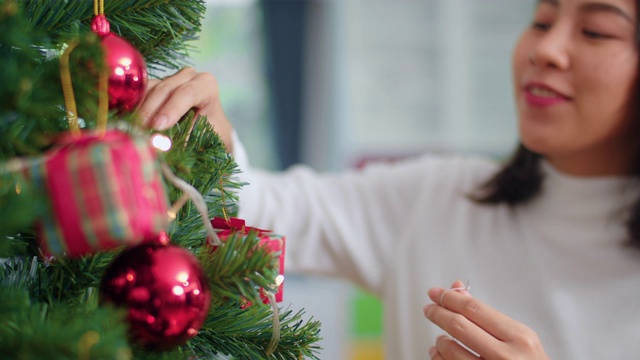 亚洲妇女在圣诞节装饰圣诞树。女少年开心地微笑着在家里的客厅里庆祝圣诞寒假。近距离和慢动作镜头。视频素材