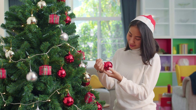 亚洲妇女在圣诞节装饰圣诞树。女少年开心地微笑着在家里的客厅里庆祝圣诞寒假。视频素材