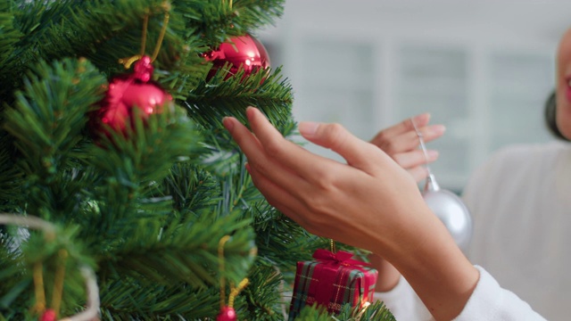 亚洲妇女在圣诞节装饰圣诞树。女少年开心地微笑着在家里的客厅里庆祝圣诞寒假。近距离射杀。视频素材