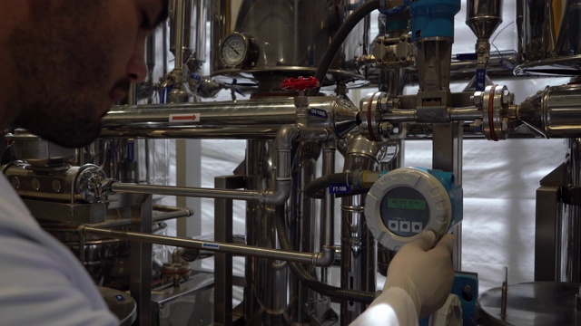 一个年轻人正在调整蒸馏厂机器的气体流量视频素材