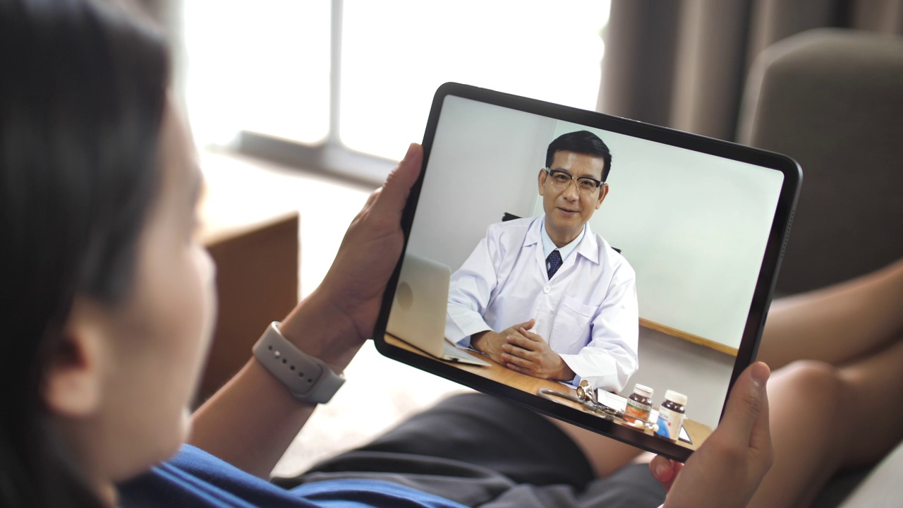 医生在家里用数码平板电脑与女病人进行视频会议视频下载
